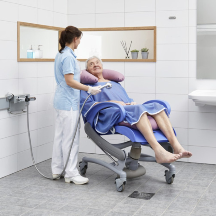 A man sitting on a Carendo Hygiene and Shower Chair while a nurse cleans him.